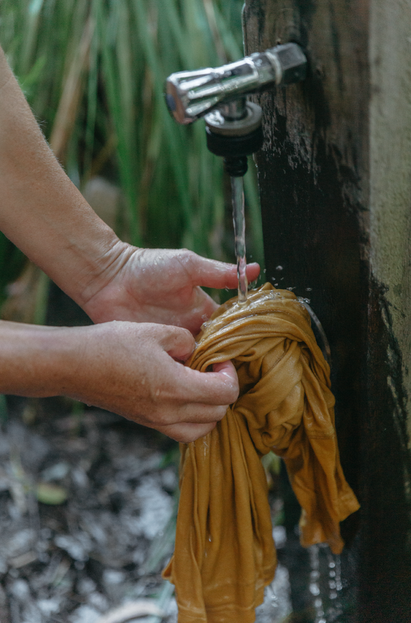 Wolf Bear Collective Origin T-Shirt in yellow colour lifestyle photo of two hands washing the tee under a fountain probably near the beach