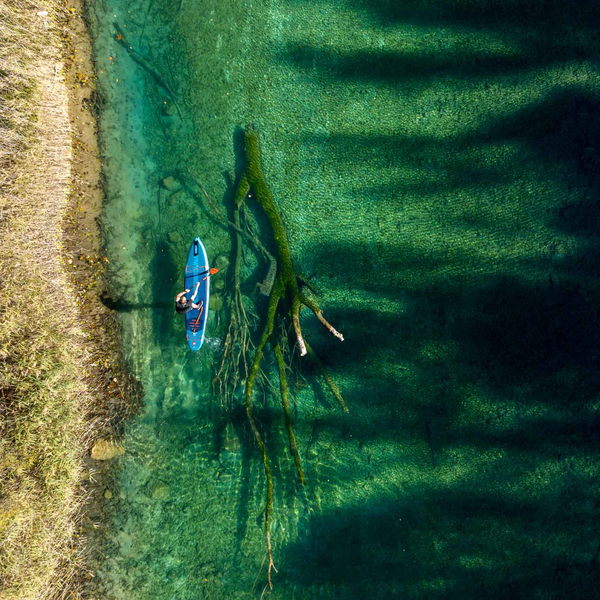 photo taken from above of a man paddle boarding across crystalline waters