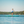 Load image into Gallery viewer, Woman paddle boarding in shorts across a very flat and blue ocean
