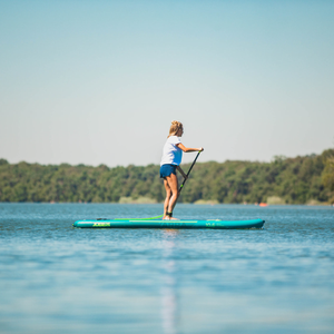 Woman paddle boarding in shorts across a very flat and blue ocean