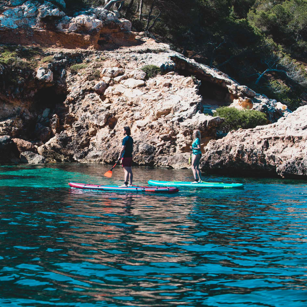 one man and a woman standing on their paddle boards near the coast